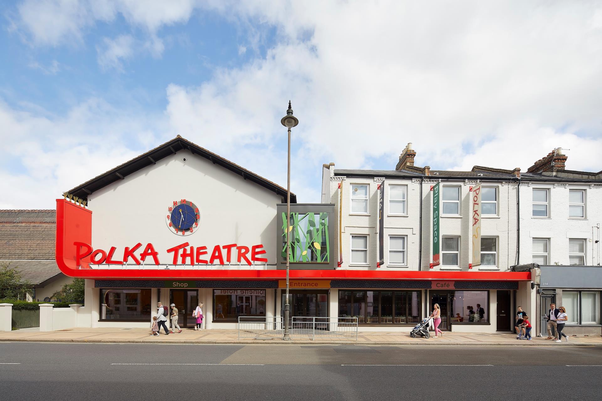 An image of Polka Theatre from the front. A white building with large red letters reading 'Polka Theatre' and a large blue and red clockface.