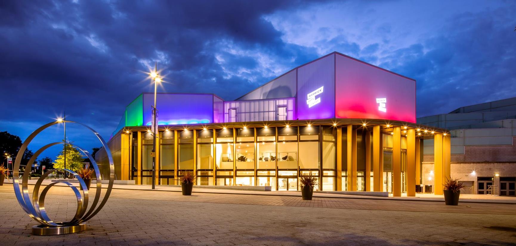 Photograph of the Warwick Arts Centre building. Lit up at night.