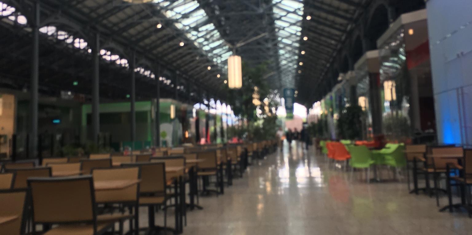 Walkway to gift shop and ticket booth. Tables and chairs are in the middle and cafes and small shops on either side.