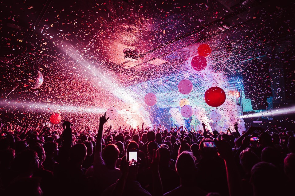 Crowd dancing to a performer with confetti and balloons